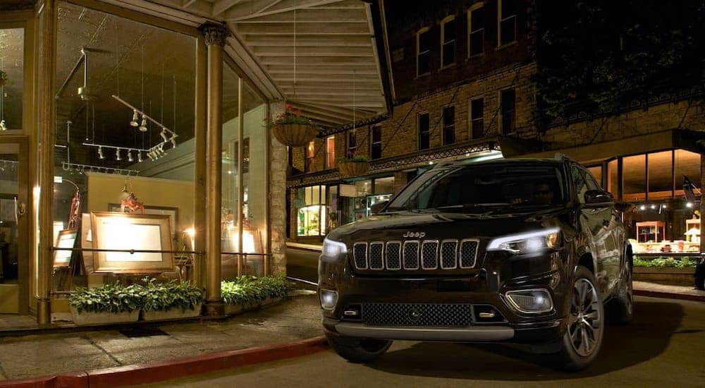 A black 2020 Jeep Cherokee is parked in front of an art gallery at night.