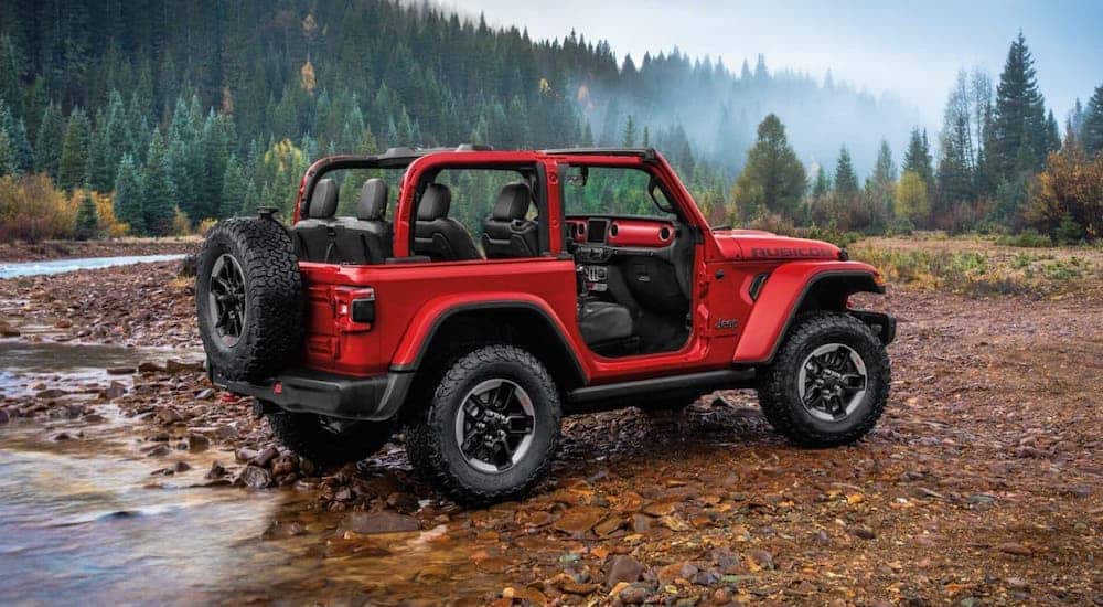 A red 2020 Jeep Wrangler Rubicon is parked on a river bank in the wilderness.