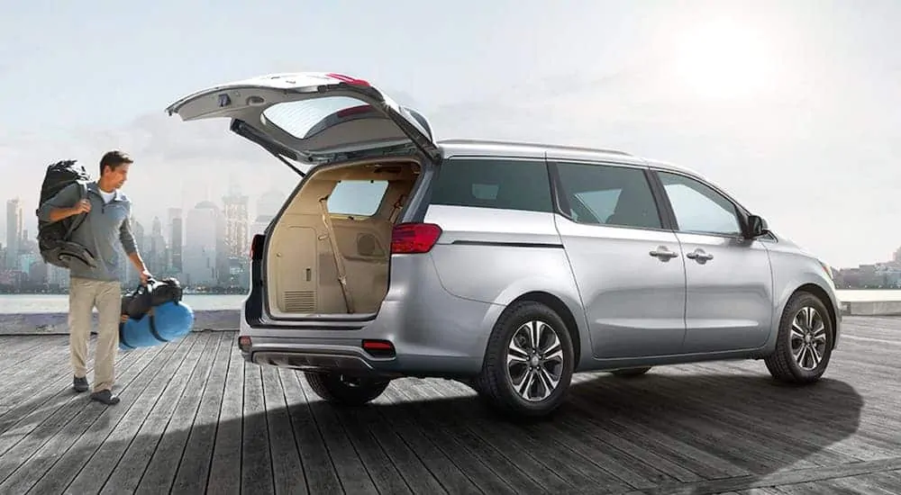 A man is loading cargo into the rear of a silver 2020 Kia Sedona that is parked on a pier.