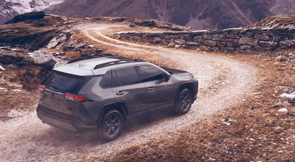 A dark grey 2020 Toyota RAV4 is driving on a winding dirt road.