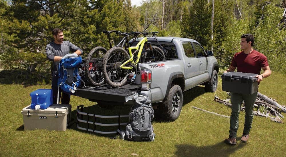 Two men are unloading mountain biking gear out of the bed of a grey 2020 Toyota Tacoma.