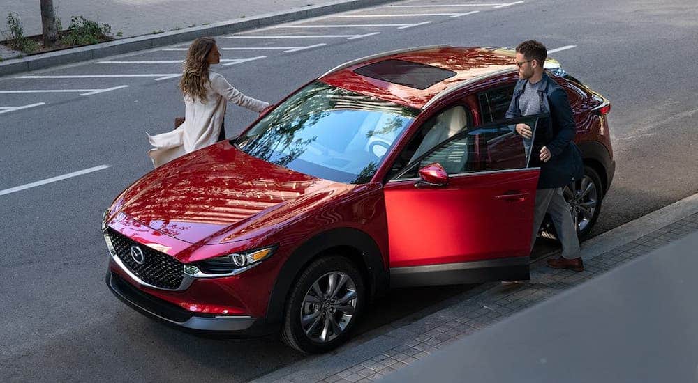 A man and a woman are getting into a red 2020 Mazda CX-30.