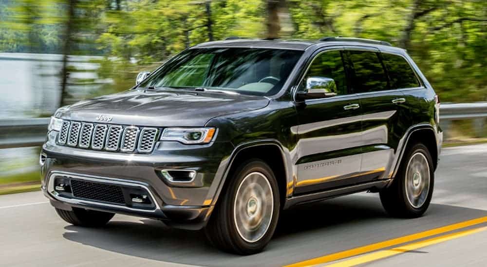 A grey 2020 Jeep Grand Cherokee is driving past green trees and a lake.
