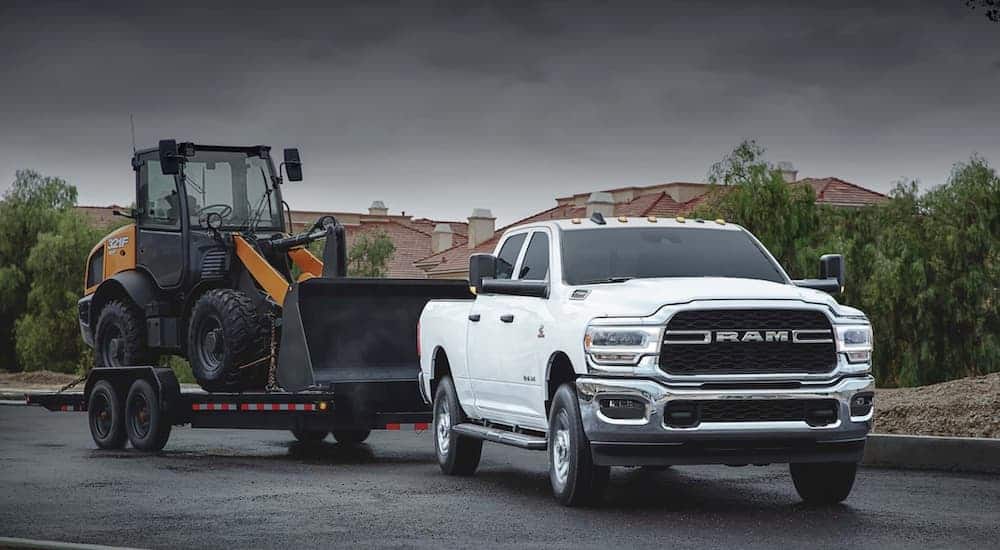 A white 2020 Ram 2500 is towing construction equipment.