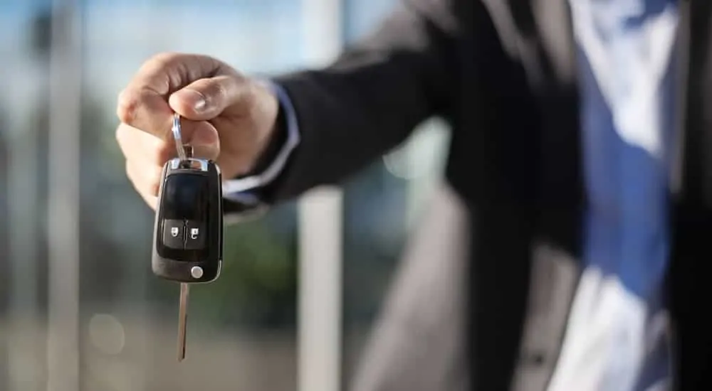 A salesman is handing over the keys to a used car.