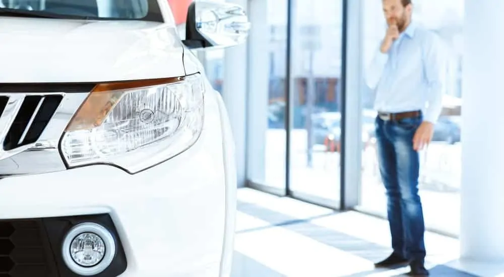 A man is in the background at a used car dealership near me looking at a white SUV.