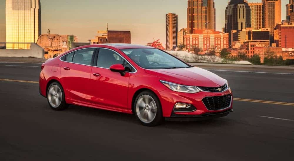 A red 2016 Chevy Cruze is driving on a highway, away from a city.