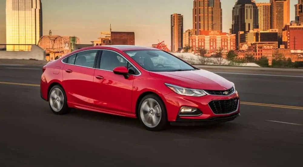 A red 2016 Chevy Cruze is driving on a highway, away from a city.