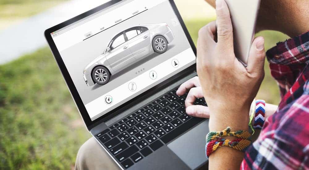 A man is researching used cars for sale on a laptop and making a phone call.