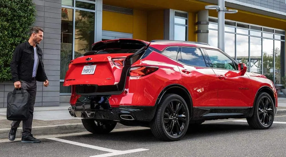 A man is opening the liftgate on a red 2020 Chevy Blazer RS on a city street.