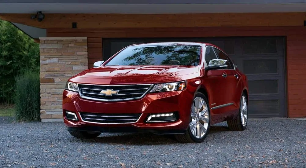 A red 2020 Chevy Impala is parked on a gravel driveway in front of a garage.