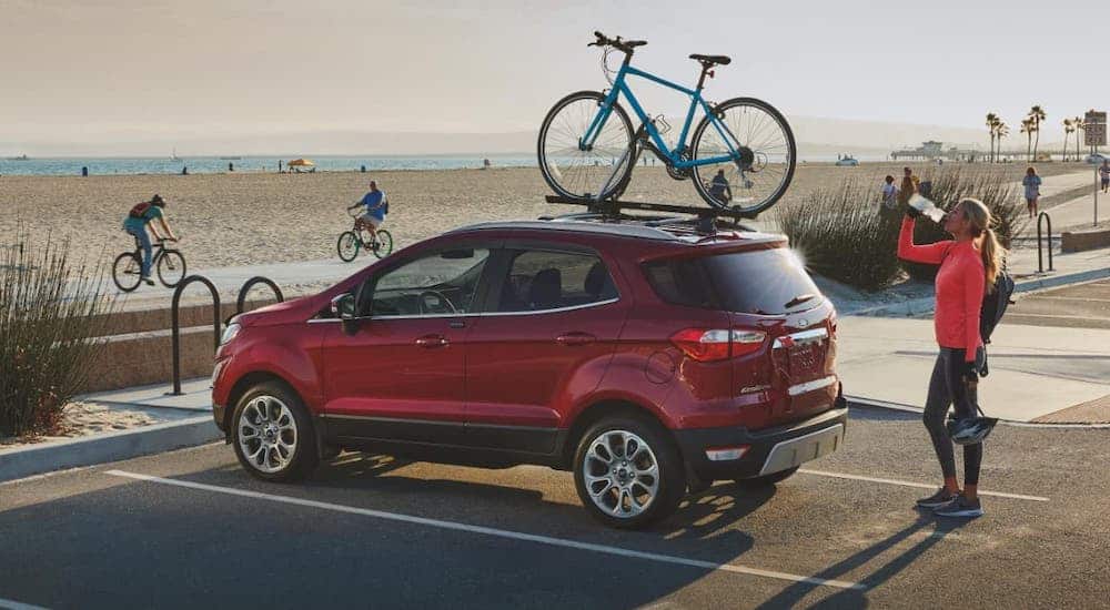 A red 2020 Ford EcoSport is parked at a beach with a bike on the roof.