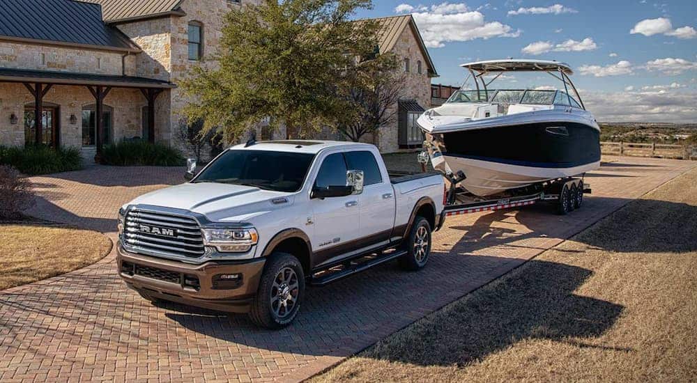 A white 2020 Ram 2500 is towing a boat past a stone house.