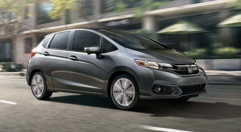 A grey 2020 Honda Fit is driving past blurred buildings.