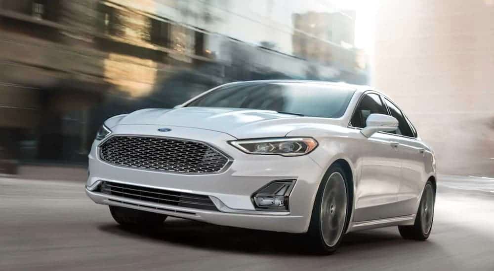 A white 2020 Ford Fusion is driving down a city street.