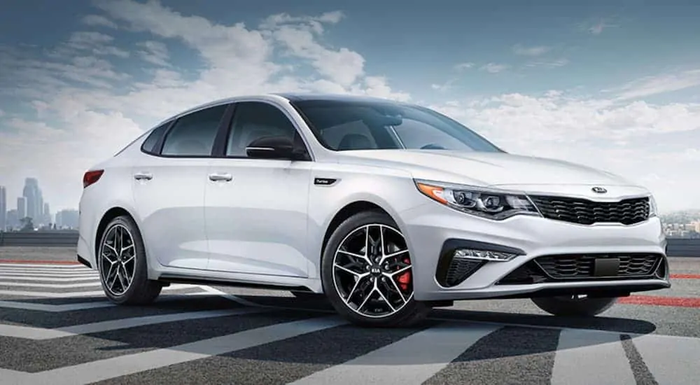 A white 2020 Kia Optima is parked with a city in the distance after winning the 2020 Kia Optima vs 2020 Ford Fusion comparison.