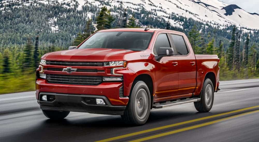 A red 2020 Chevy Silverado 1500 is driving past a snowy mountain.