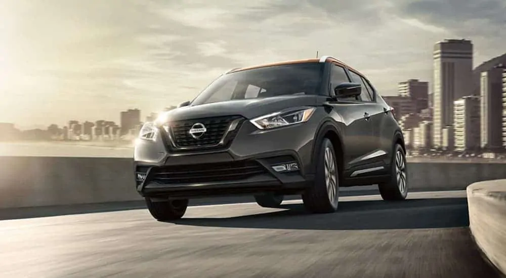 A grey 2020 Nissan Kicks is driving away from a city.