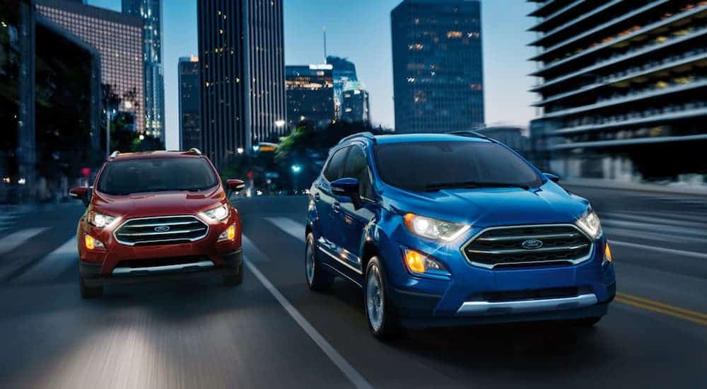 A red and a blue 2020 Ford EcoSport are driving through a city at night.