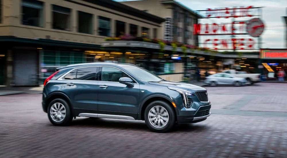 A blue/gray 2020 Cadillac XT4 from a Cadillac dealer near me is driving past a public market.