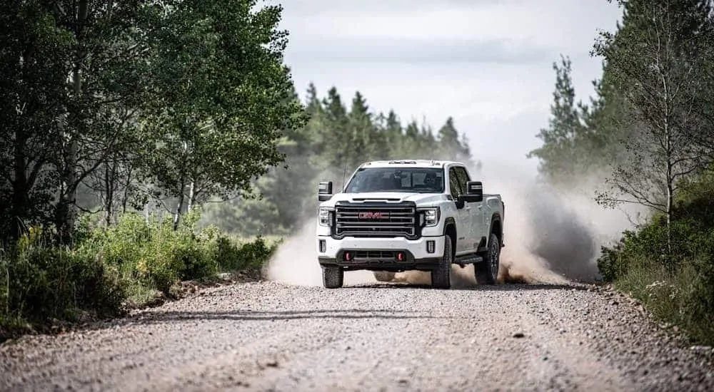 A white 2020 GMC Sierra 2500HD AT4 is kicking up dirt on a dirt road.