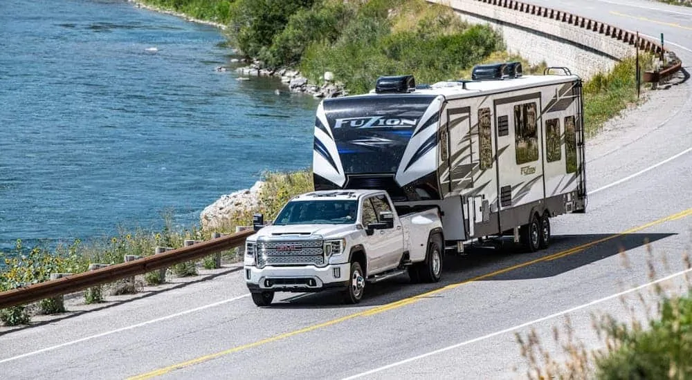 A king among GMC trucks, a white 2020 GMC Sierra 3500HD Denali is towing a large camper along a lake-side highway.