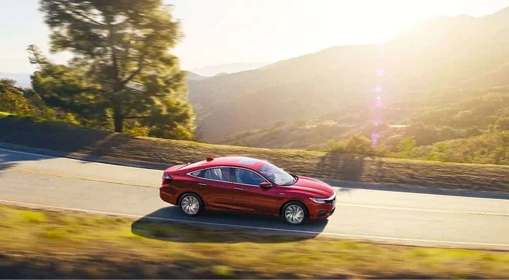 A red 2021 Honda Insight Touring is leaving a Honda dealer near me and driving through a valley at sunset.