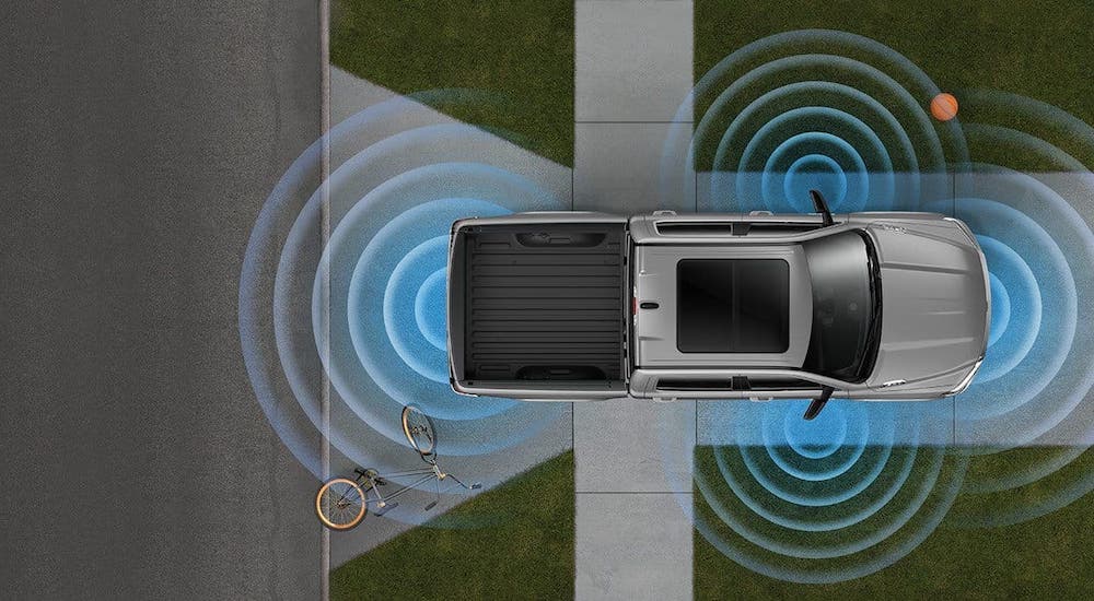 A 2020 Ram 1500 with simulated safety sensors is shown from above and backing out of a driveway.