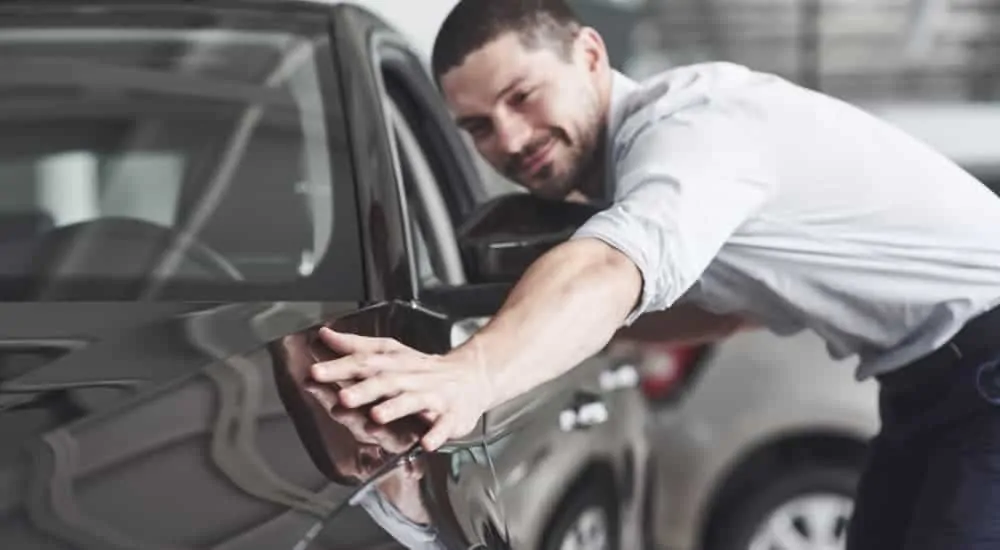 A man is looking at the fender of a black car.