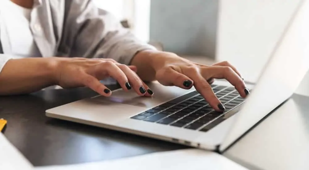 A close up is shown of a woman typing on a laptop.