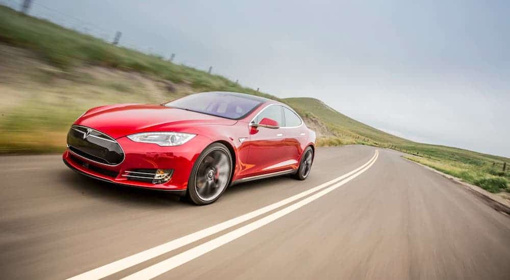 A red 2015 Tesla Model S is driving on a country highway.