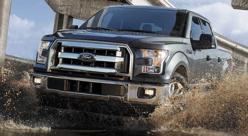A used blue 2017 Ford F-150 XLT is splashing through a puddle of mud.