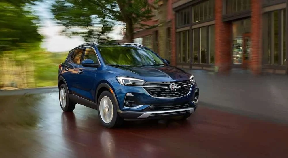 A blue 2020 Buick Encore GX is driving around a corner in front of a brick building after winning the 2020 Buick Encore GX vs 2020 BMW X1 comparison.