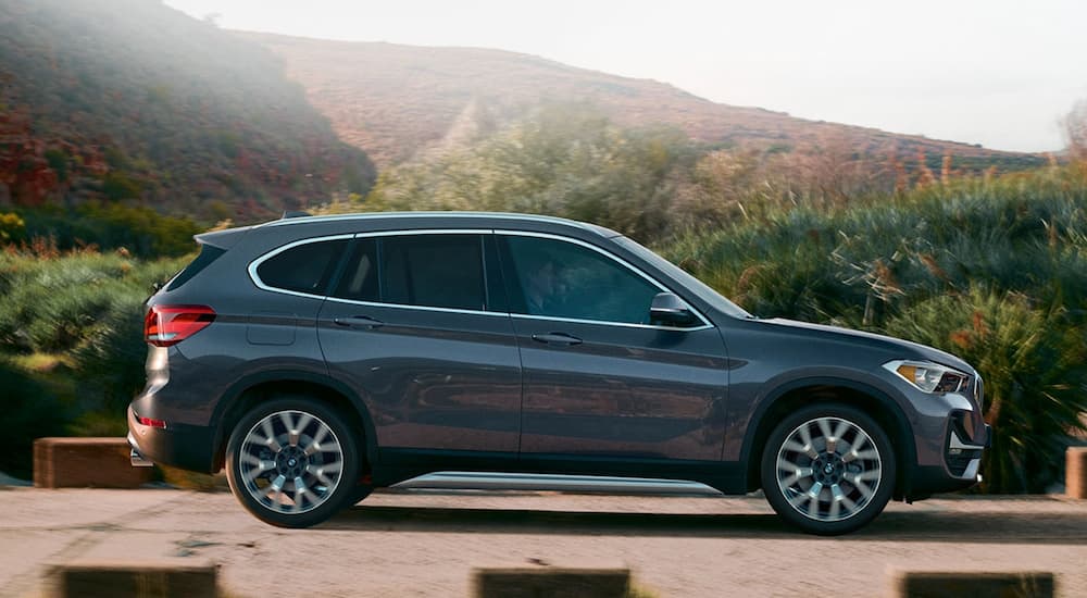 A grey 2020 BMW X1 is shown from the side in front of hills and trees.