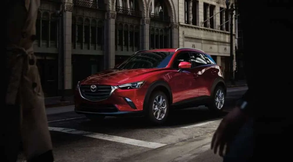 A red 2020 Mazda CX-3 is stopped on a busy, dark city street.