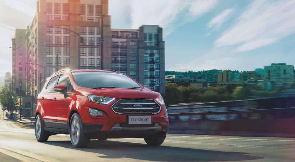 A red 2020 Ford EcoSport is driving away from a city after winning the 2020 Ford EcoSport vs 2020 Buick Encore comparison.