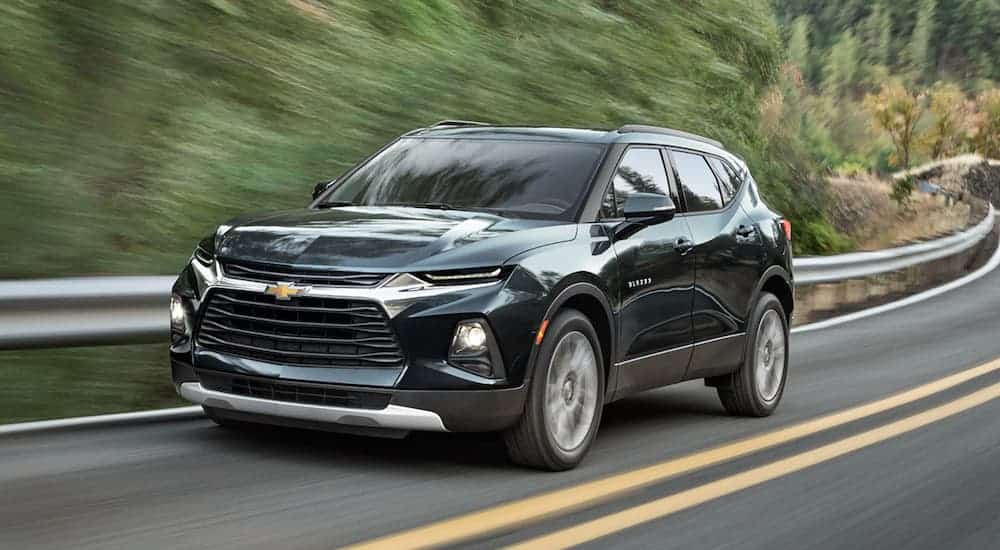 A dark green 2020 Chevy Blazer is driving past a guard rail and trees.