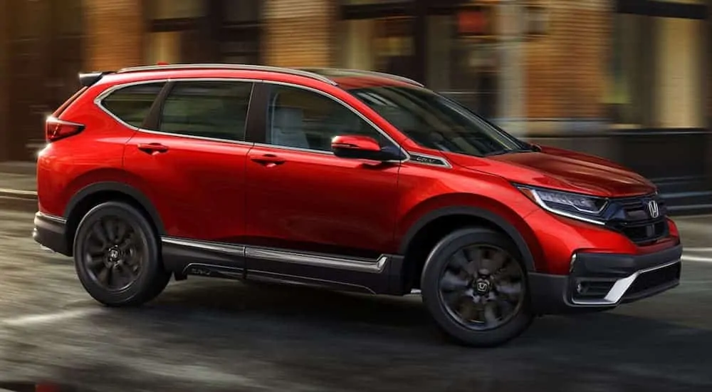 A red 2020 Honda CR-V Touring is driving around a corner on a city street.