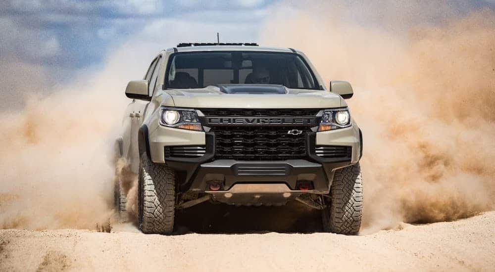 A tan 2021 Chevy Colorado ZR2 is shown from the front and kicking up sand on a trail.