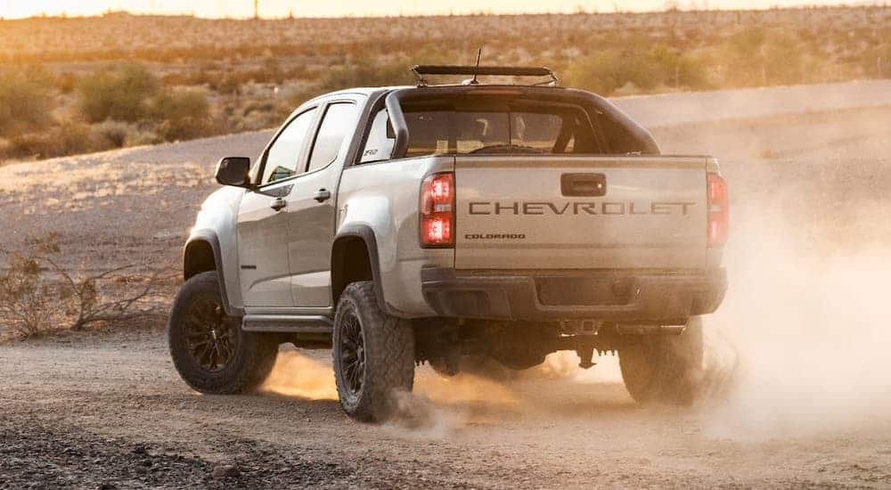 A tan 2021 Chevy Colorado ZR2 is kicking up dirt on a trail at sunset.