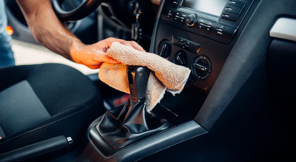 The shifter on a leased car is being cleaned with an orange cloth.