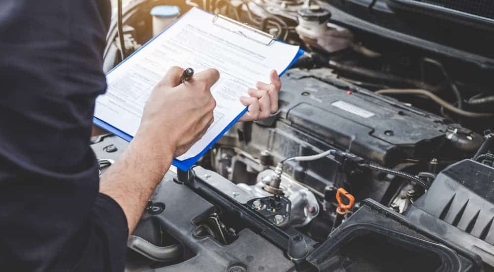 A mechanic is holding a clipboard and checklist in front of an engine bay.