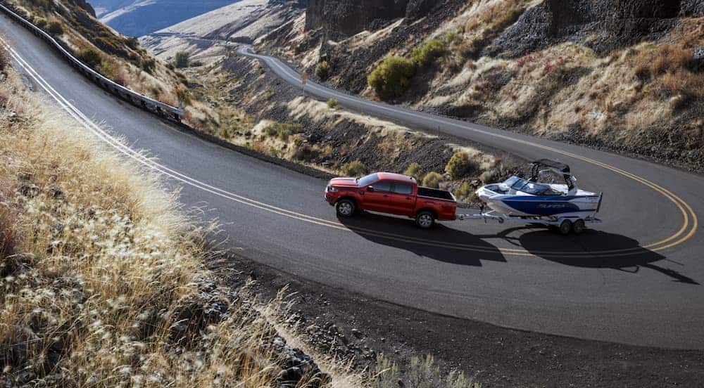 A red 2020 Ford Ranger is towing a boat on a winding mountain road.