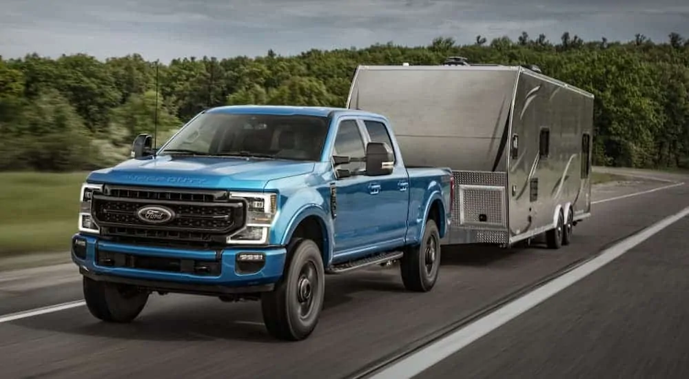 A blue 2020 Ford Super Duty is towing a camper on a cloudy day.
