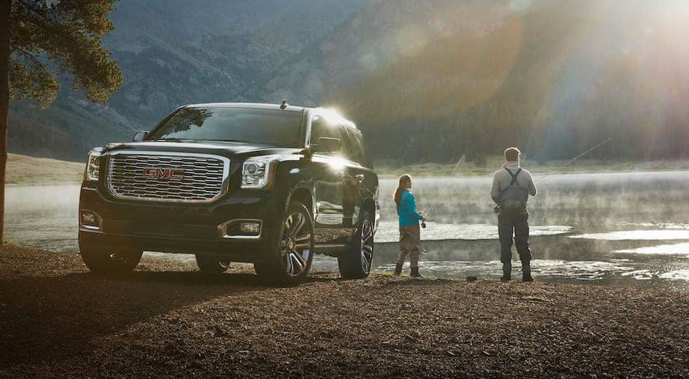 A couple is fishing at a lake next to a black 2020 GMC Yukon.