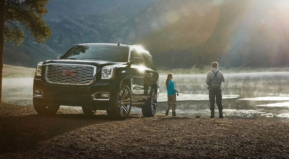 A couple is fishing at a lake next to a black 2020 GMC Yukon.