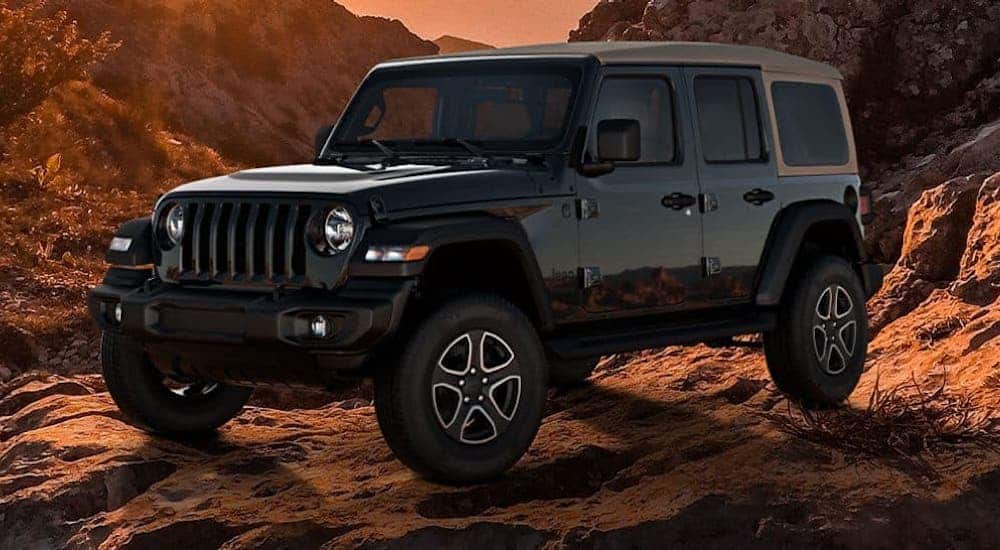 A black 2020 Jeep Wrangler Unlimited Black And Tan edition is parked on rocks at dusk.