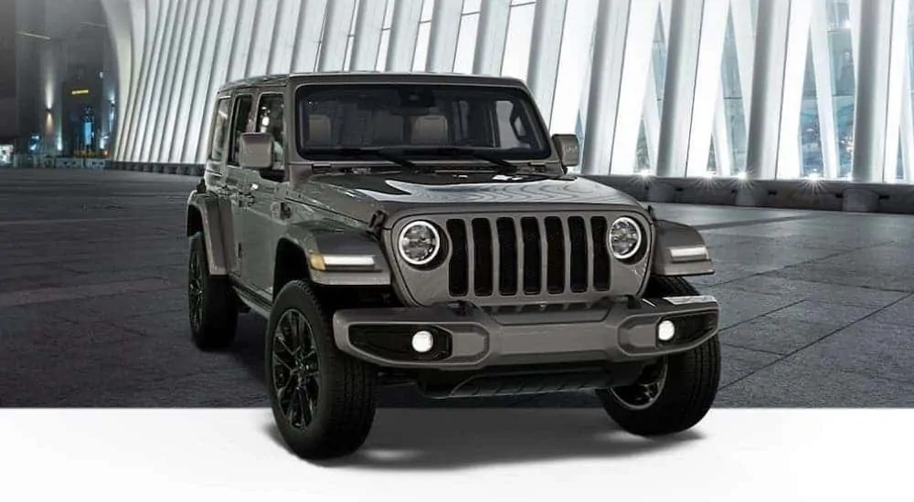 A dark gray 2020 Jeep Wrangler Unlimited High Altitude edition is parked in front of a glass building at night.