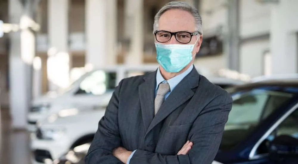 A car salesman with a face mask is standing in a car showroom.