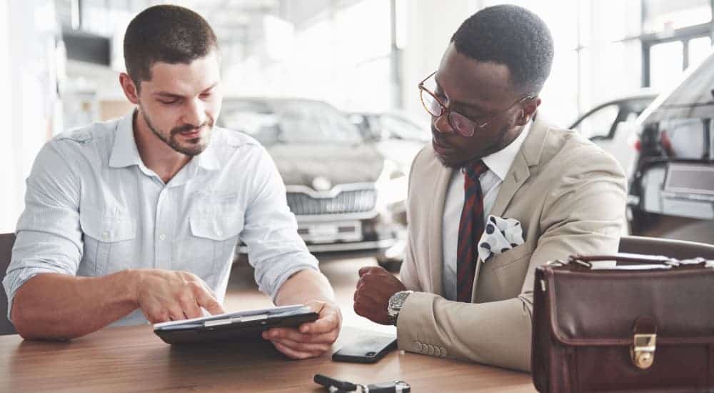 A salesman and a customer are looking at a tablet at a car dealership.